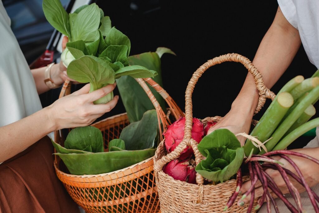pexels-photo-5709305-5709305 Close-up of hands holding wicker baskets filled with fresh vegetables and fruits outdoors.